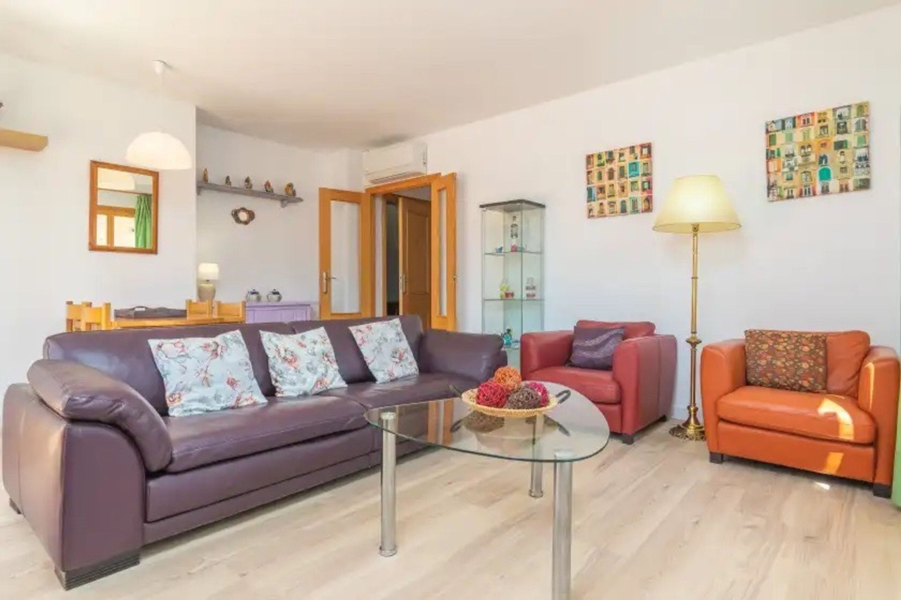 A living room with a glass coffee table, a purple sofa, a red armchair, and an orange sofa.