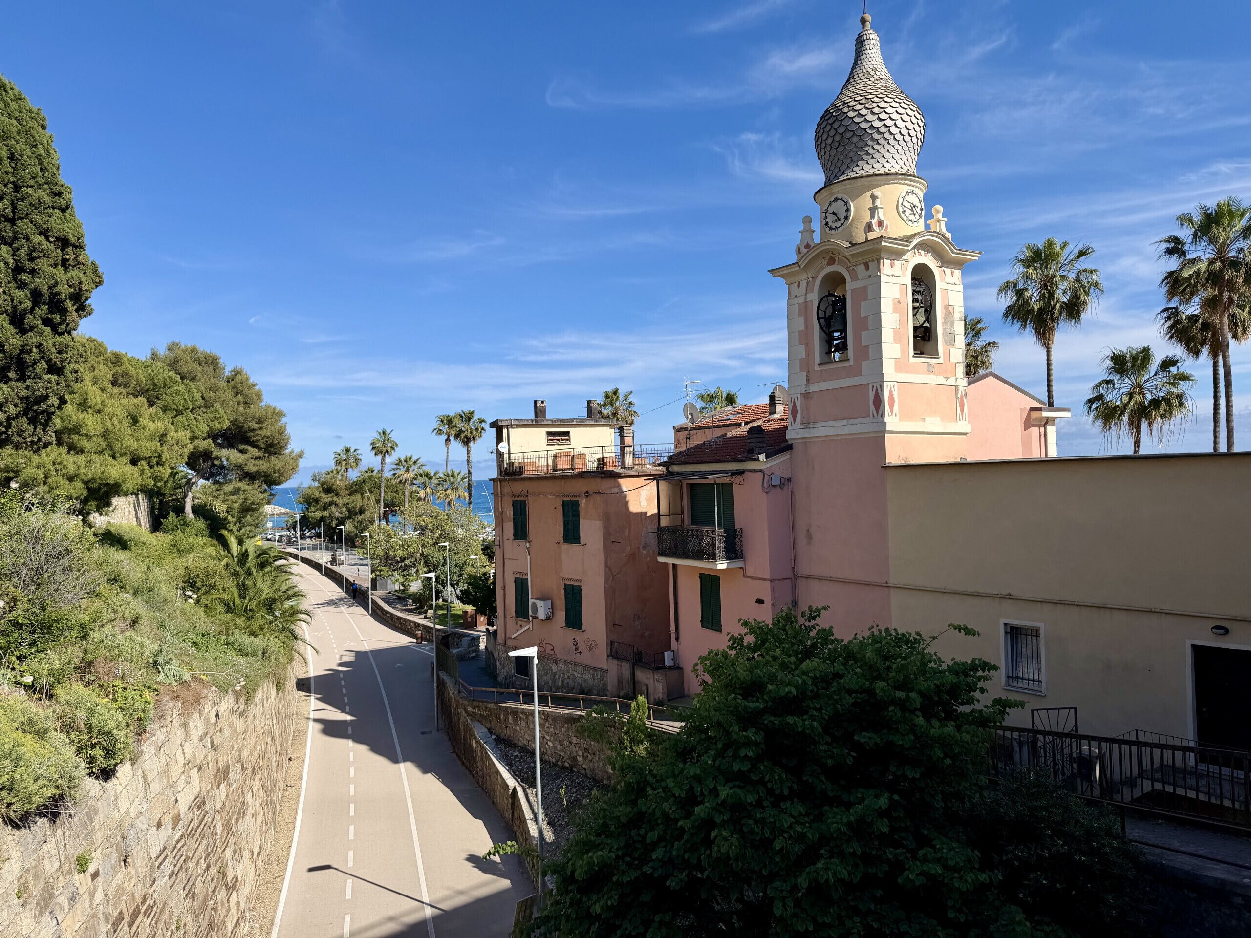 A coastal town with a prominent clock tower, a paved road, and lush greenery.
