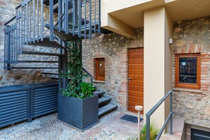 Un edificio de piedra con puerta de madera, una escalera con barandillas de metal y una jardinera con plantas.
