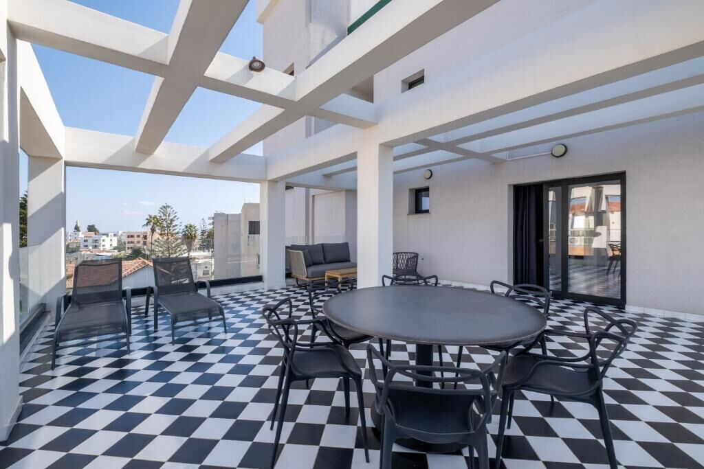 A rooftop terrace with a checkered floor, outdoor seating, and a view of the cityscape.