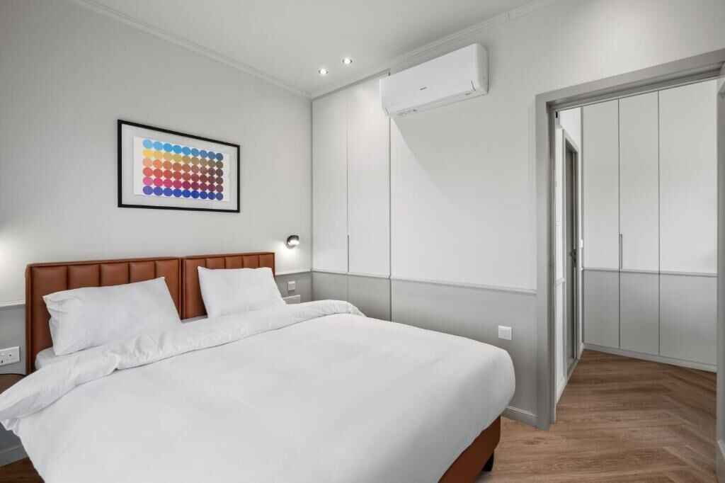 A bedroom with a bed, a framed artwork, an air conditioning unit, and a wardrobe.