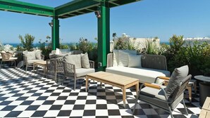 An outdoor patio with checkered flooring, green metal beams, and outdoor furniture.