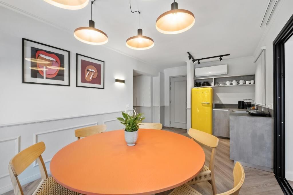 Eine moderne Küche mit einem gelben Kühlschrank, einem Essbereich mit einem runden orangefarbenen Tisch und Pendelleuchten.