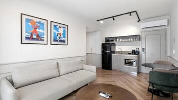 Uma sala de estar moderna com um sofá, uma mesa de centro e uma cozinha ao fundo.