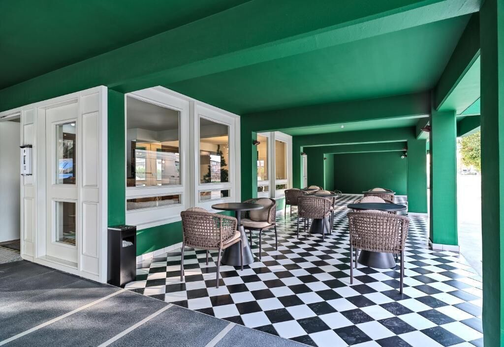A covered outdoor seating area with checkered flooring, wicker chairs, and a view of the street.