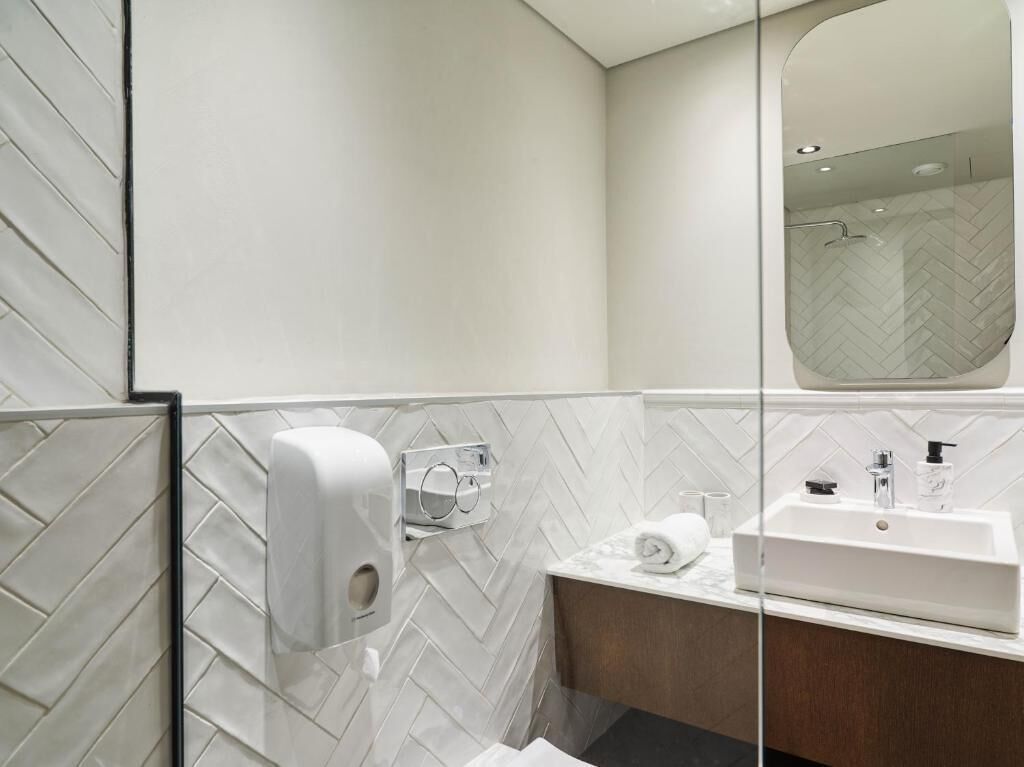 Een moderne badkamer met een handdroger, een handdoekdispenser en een wastafel met spiegel.
