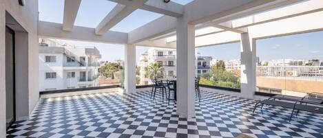 Una terraza en la azotea con suelo a cuadros, mobiliario exterior y vistas de edificios circundantes.