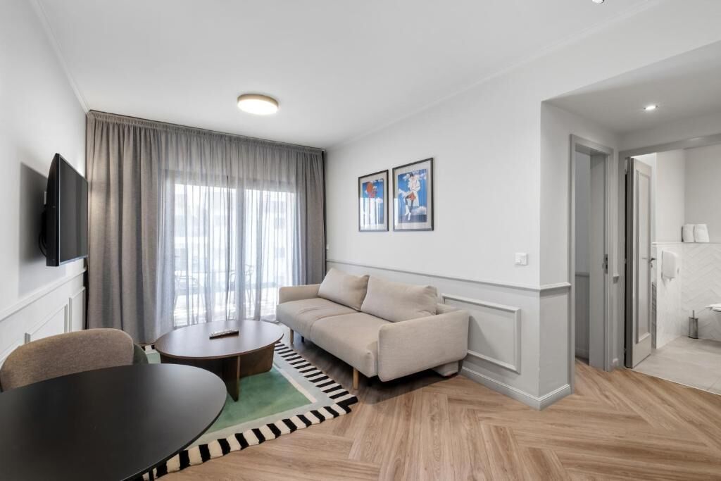 A modern living room with a sofa, a TV, a dining table, and a large window with curtains.