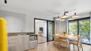 A modern kitchen with a dining area, large windows, and a view of greenery.