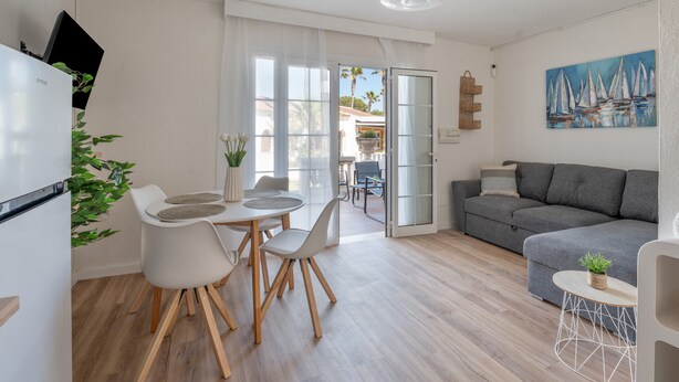 Un espace de vie moderne comprenant un coin repas, un canapé gris et un tableau représentant des voiliers.