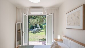 Une chambre à coucher avec un lit, une table de chevet, un tableau encadré et une porte ouverte donnant sur un jardin.