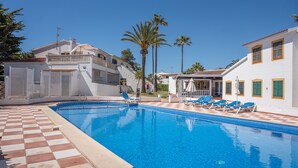 Une piscine entourée de chaises longues, une terrasse à motifs à carreaux et un bâtiment doté de balcons, avec des palmiers en arrière-plan.