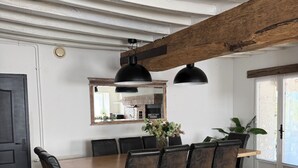 Een eetruimte met een houten tafel, zwarte stoelen, een grote spiegel en een hangende lamp.