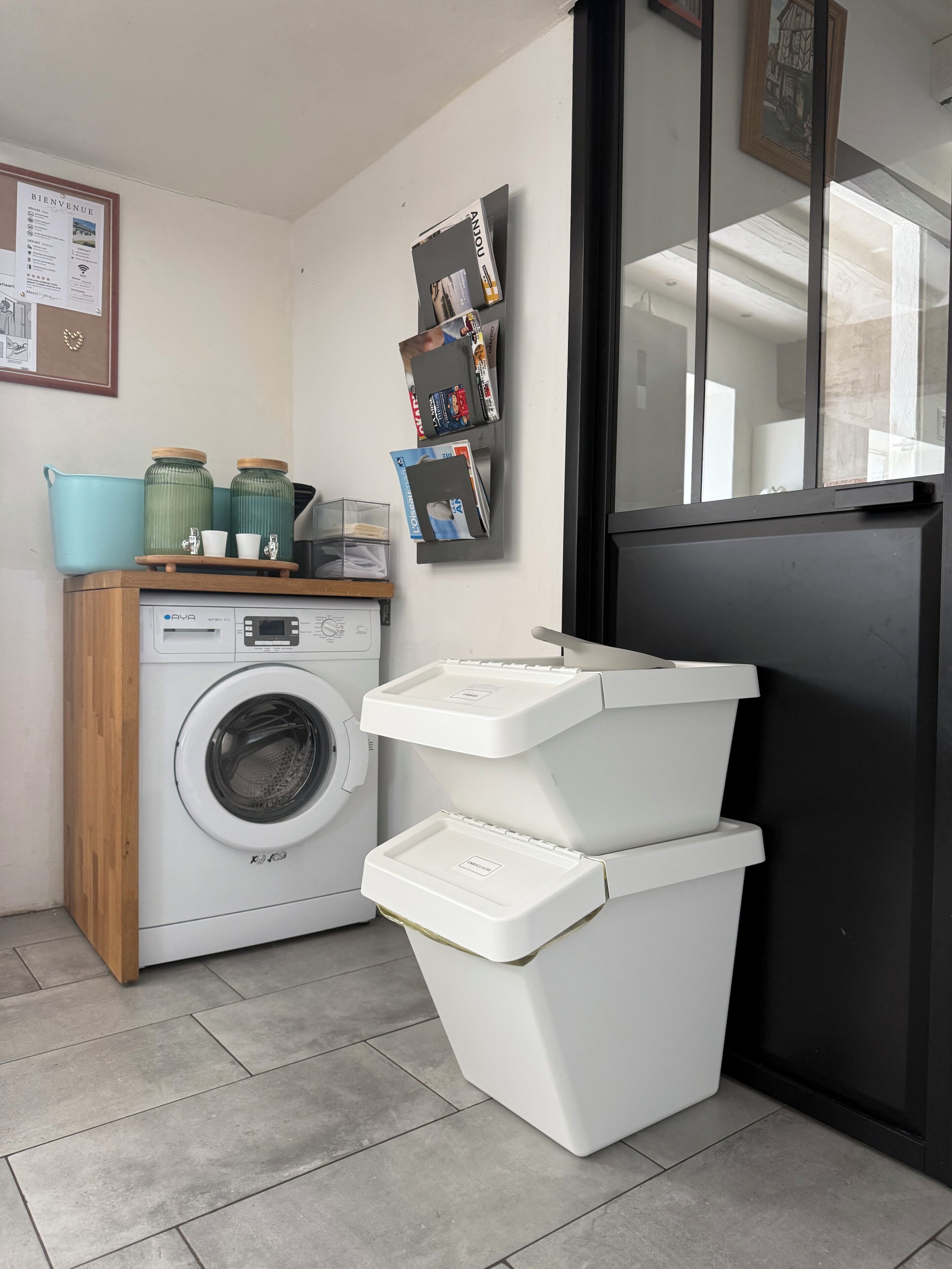 A laundry area with a washing machine, stacked bins, and a welcome sign.