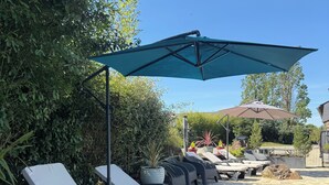 Een terras met loungestoelen, een stenen pad en een grote parasol.