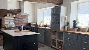 Een moderne keuken met een groot eiland, grijze kastjes, een bakstenen muur en een raam met uitzicht.