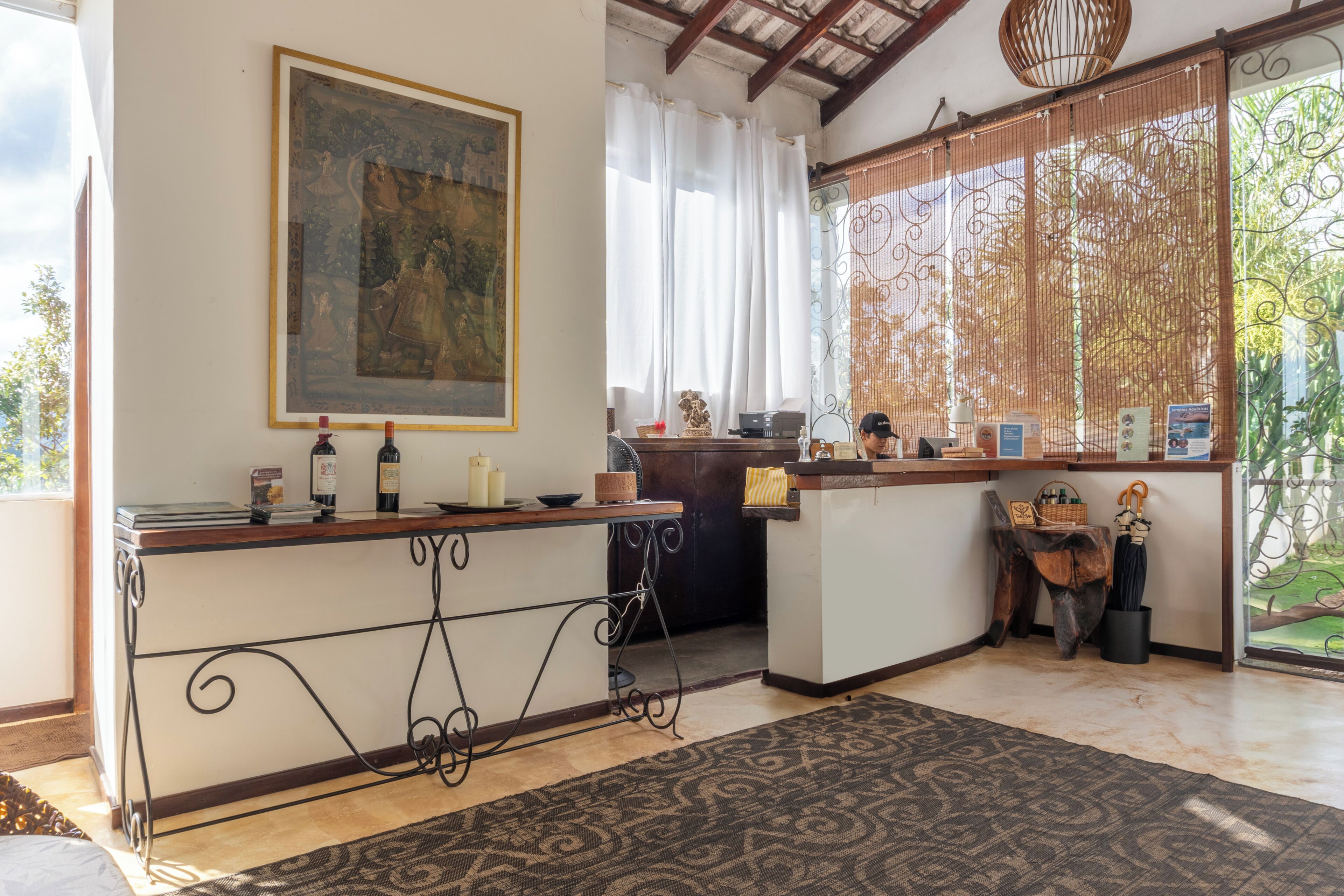 A room with a wooden counter, a painting on the wall, a patterned rug, and a view through a bamboo screen.