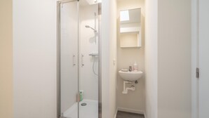 Un baño con cabina de ducha de vidrio, un lavabo blanco y un espejo encima.