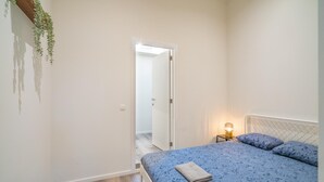 Un dormitorio con cama, lámpara de noche y una puerta que da a otra habitación.