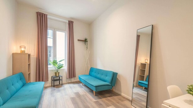Una habitación con dos sofás, un espejo, una mesita, una planta en maceta y una ventana con cortinas.