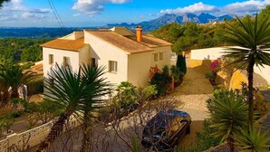 A two-story house with a tiled roof, surrounded by greenery and a clear view of mountains in the background. - Villa Margarita - Altea’s Pure Delight (Altea)