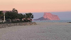 A pebble beach with a rocky outcrop in the distance, palm trees, and a building with a lamp post. - Villa Margarita - Altea’s Pure Delight (Altea)