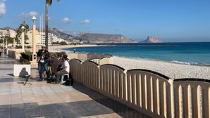 Une promenade en bord de mer, avec un palmier, une clôture blanche et une plage en arrière-plan.