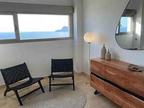 Une pièce avec une grande fenêtre, un lampadaire rond, un miroir et une commode en bois.