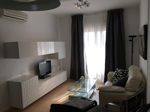 Ein modernes Wohnzimmer mit einem Flachbildfernseher, einem Glastisch, einer Couch und einer weißen Kommode.