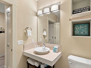 A bathroom with a white sink, a mirror, and a toilet. There are towels hanging on the wall and a sign that says 'Relax, you're at the beach.' - One Bedroom Condo at Bahia in Sandestin Golf and Beach Resort (Miramar Beach)