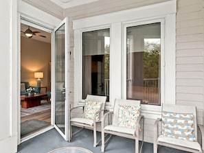 A covered porch with three chairs, a table, and a view of the interior. - One Bedroom Condo at Bahia in Sandestin Golf and Beach Resort (Miramar Beach)