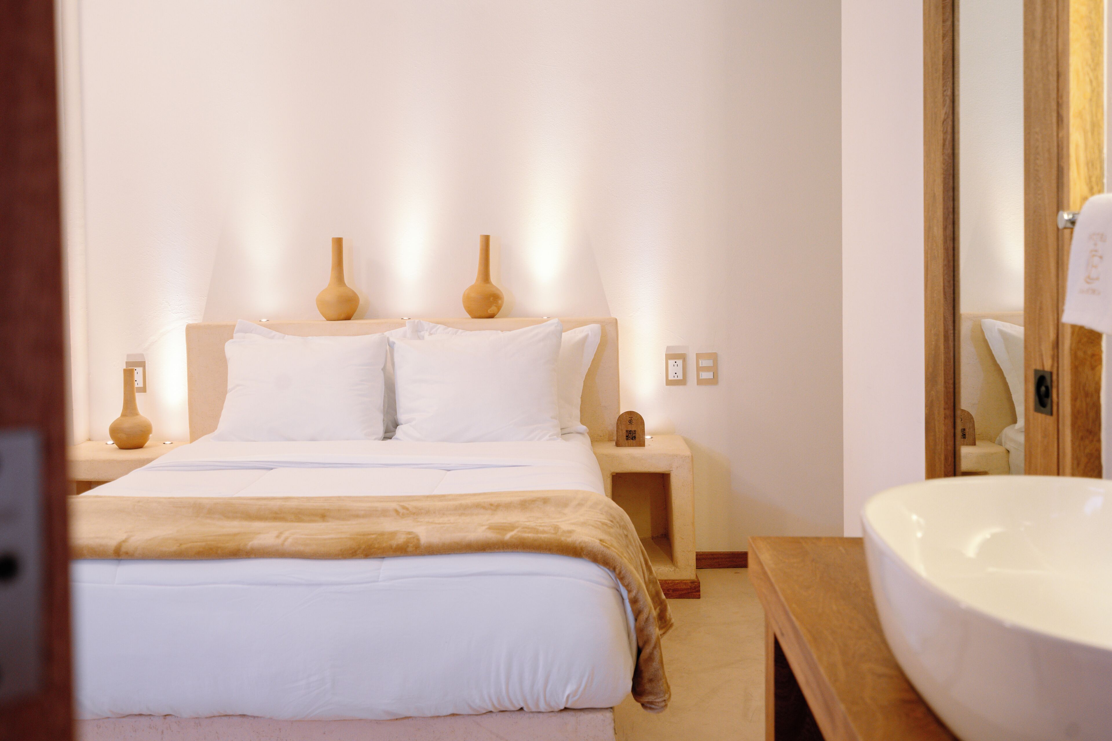 A bedroom with a bed, bedside tables, a nightstand, a mirror, and a large white sink.