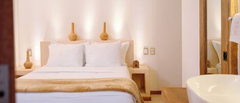 A bedroom with a bed, bedside tables, a nightstand, a mirror, and a large white sink.