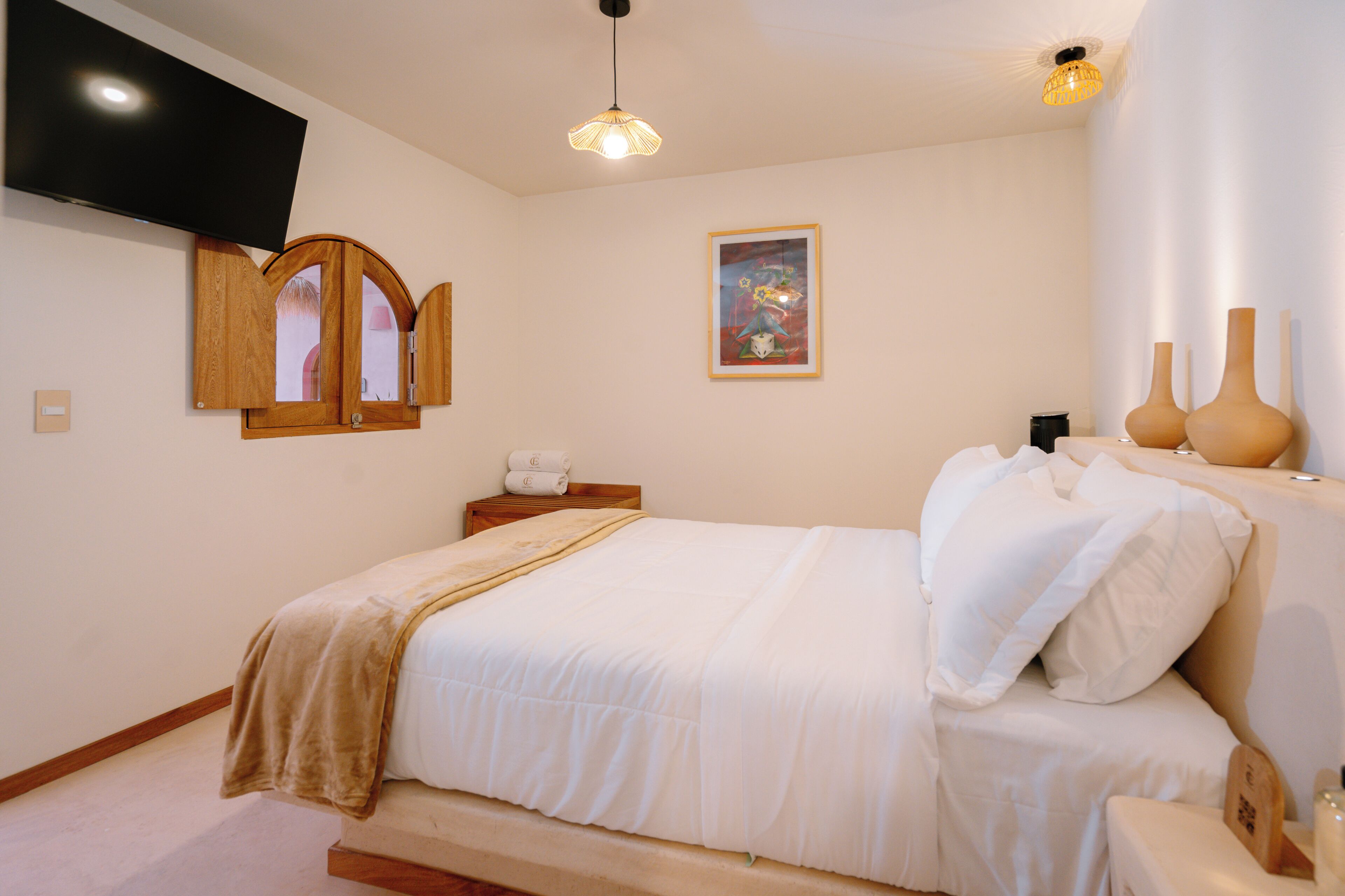 A bedroom with a bed, a television mounted on the wall, a bedside table with a lamp, and a framed picture on the wall.