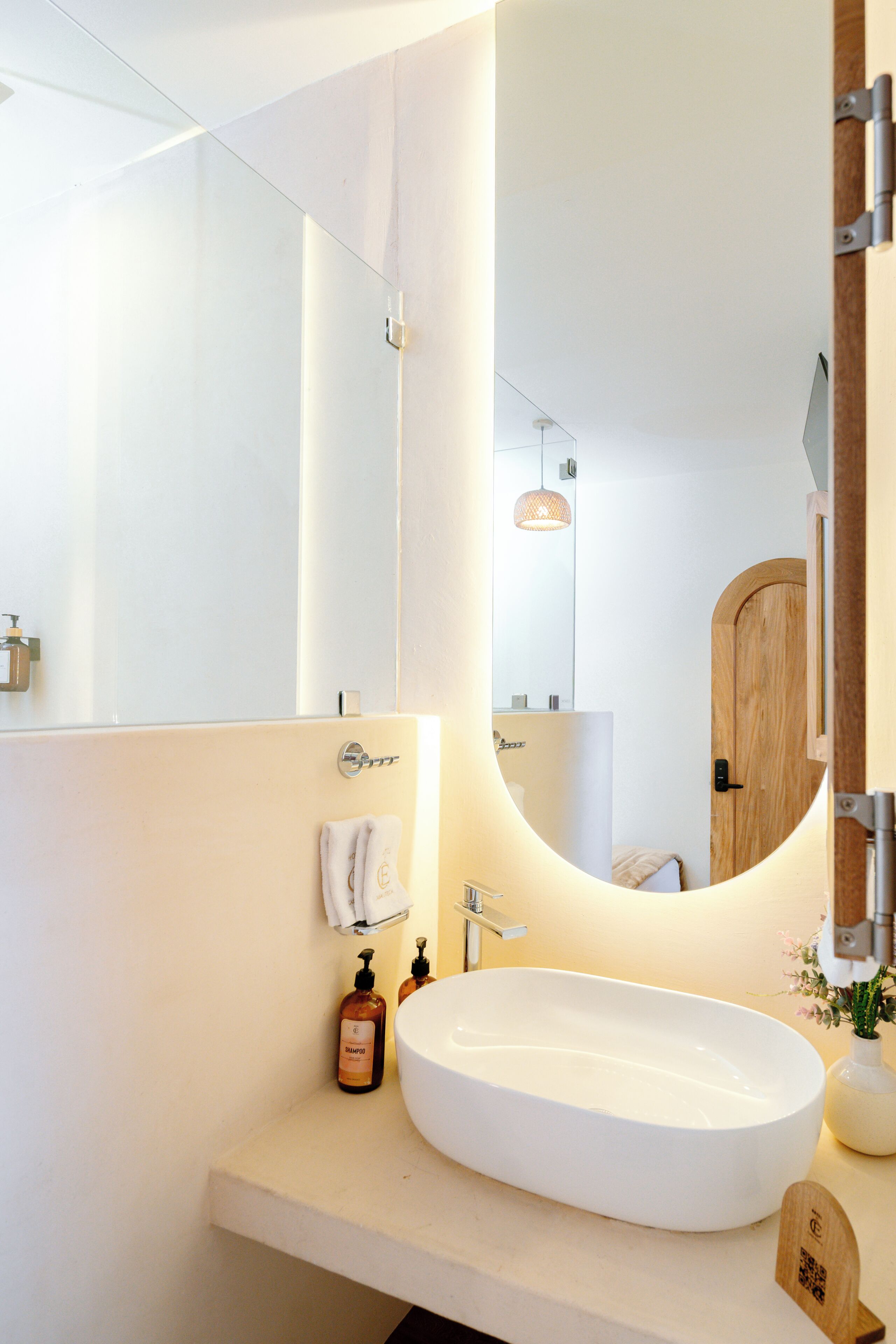 Un bany modern amb un mirall gran, un lavabo rodó i una porta de fusta.