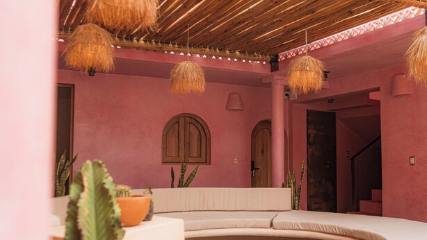 Una stanza dalle pareti rosa con un letto a forma di ferro di cavallo, porte in legno e lampade a sospensione.