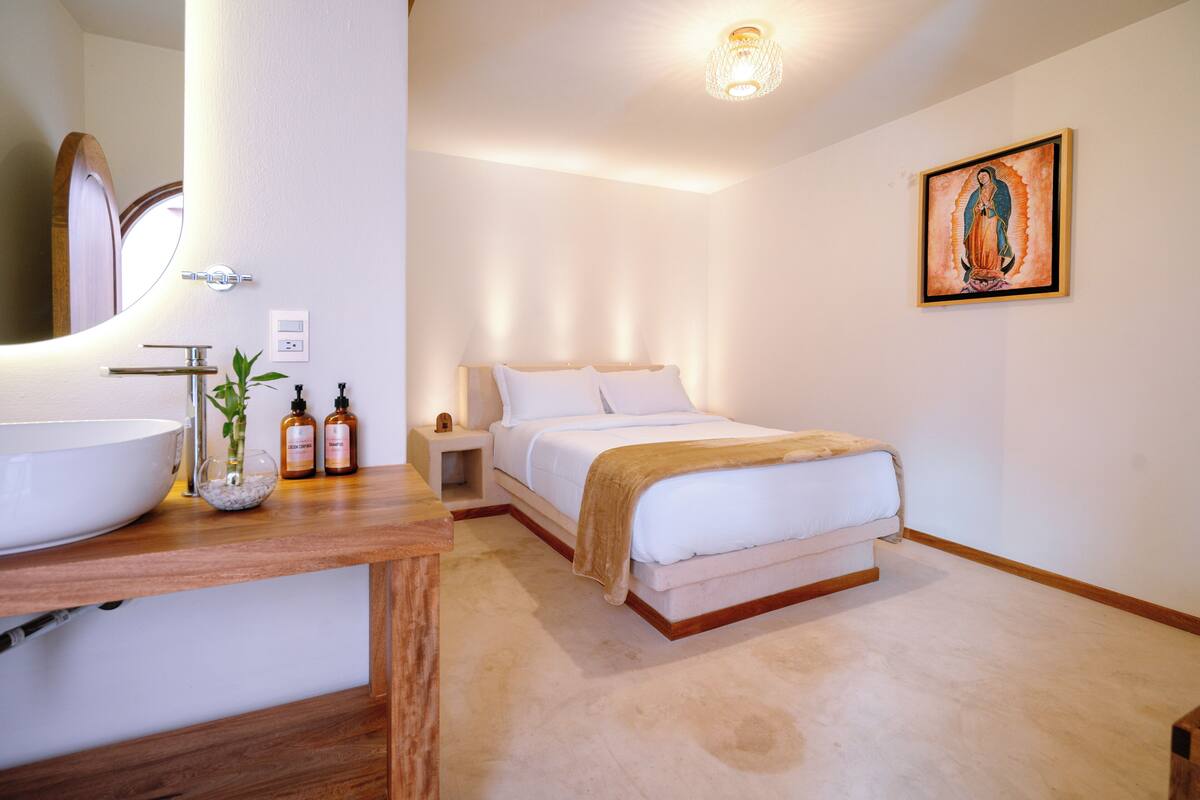 A bedroom with a large bed, a wooden bedside table, a nightstand, a white sink, and a mirror.