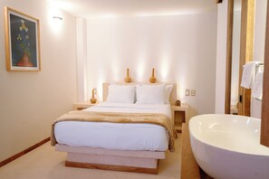 Ein Schlafzimmer mit einem großen Bett, Nachttischen, einem Gemälde und einer Badewanne.