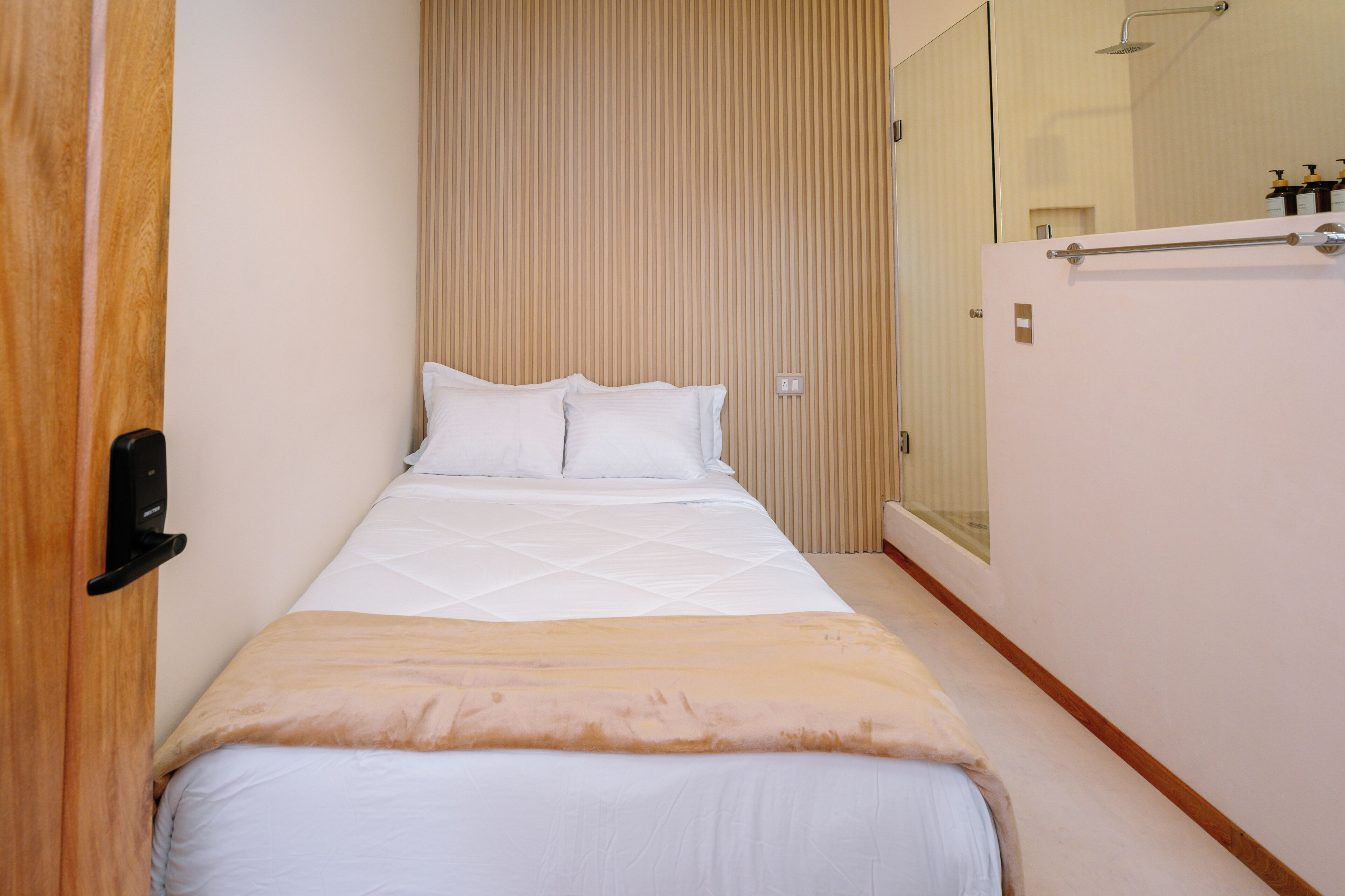A narrow hotel room with a bed, a wooden door, and a mirror.