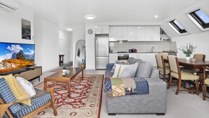 En moderne lejlighed med opholdsstue, spiseplads, køkken og et fjernsyn, der viser et bjerglandskab.