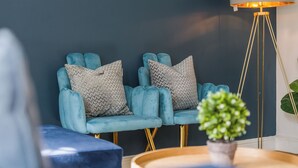 Una habitación con una pared azul oscuro, dos sillones azules con cojines estampados, una lámpara de pie y una pequeña planta en maceta.