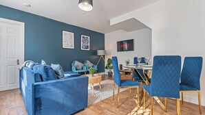 Una sala de estar moderna con un sofá azul, sillas a juego, una mesa de comedor y un televisor instalado en la pared.