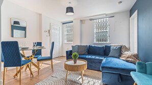 Una sala moderna con un sofá azul, sillas a juego, una mesa de centro redonda y un comedor con una mesa y sillas de vidrio.