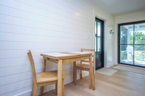 Una stanza con un tavolo e sedie in legno, una porta scorrevole in vetro e vista sul verde circostante.