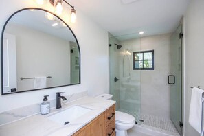 Un bagno moderno con uno specchio grande, due lavandini, un water e una cabina doccia in vetro.