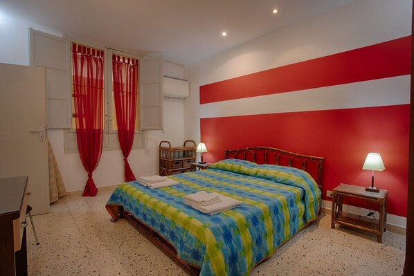 A bedroom with a bed, two bedside tables with lamps, a wardrobe, and a window with red curtains. - Cozy 80 sq m apartment, comfortably accommodating up to 4 people, located on the first floor of a period building with NO lift. The property is located in the heart of Trapani's historic center (limited traffic zone), ideally positioned for reaching all  (Trapani)