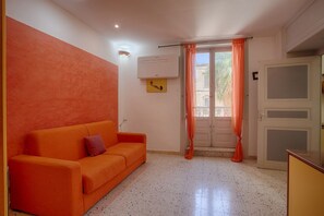 Ein Zimmer mit einer Couch, einer Tür, einer Klimaanlage und einem Fenster mit Vorhängen.