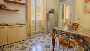 Eine Küche mit Esstisch, Stühlen, einem Kühlschrank und einem Fenster mit Vorhängen.