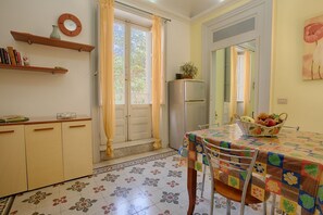 Eine Küche mit Esstisch, Stühlen, einem Kühlschrank und einem Fenster mit Vorhängen.