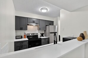 A modern kitchen with grey cabinets, a white countertop, a built-in oven, a refrigerator, and a coffee maker. - Contemporary 2BR apartment with workspace (Lenexa)